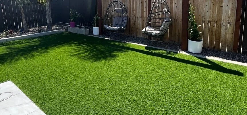Backyard with manicured grass, a wooden privacy fence, two hanging egg chairs with cushions, and potted plants.