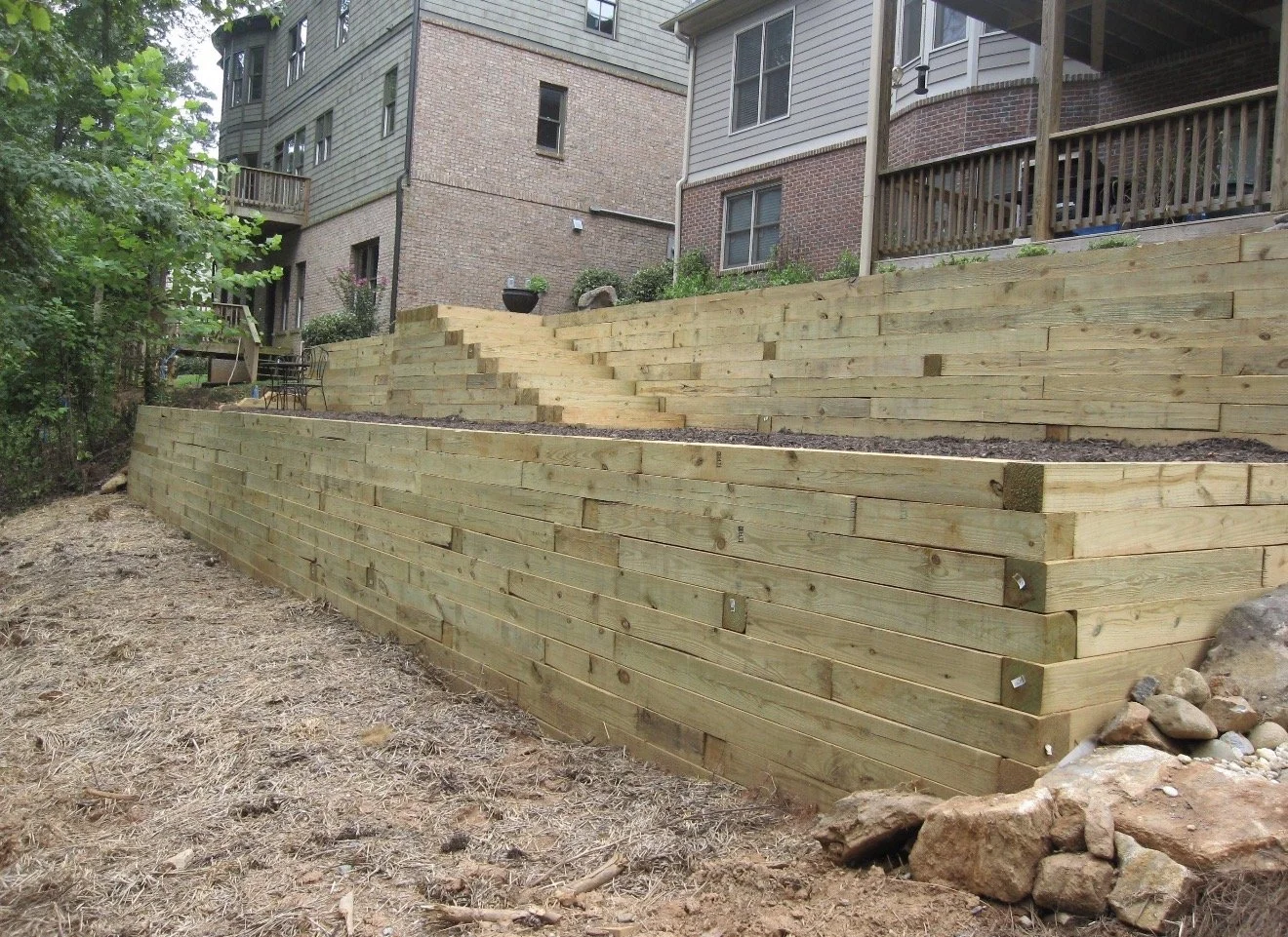 A multi-level wooden retaining wall constructed with horizontal timber planks in a residential backyard.
