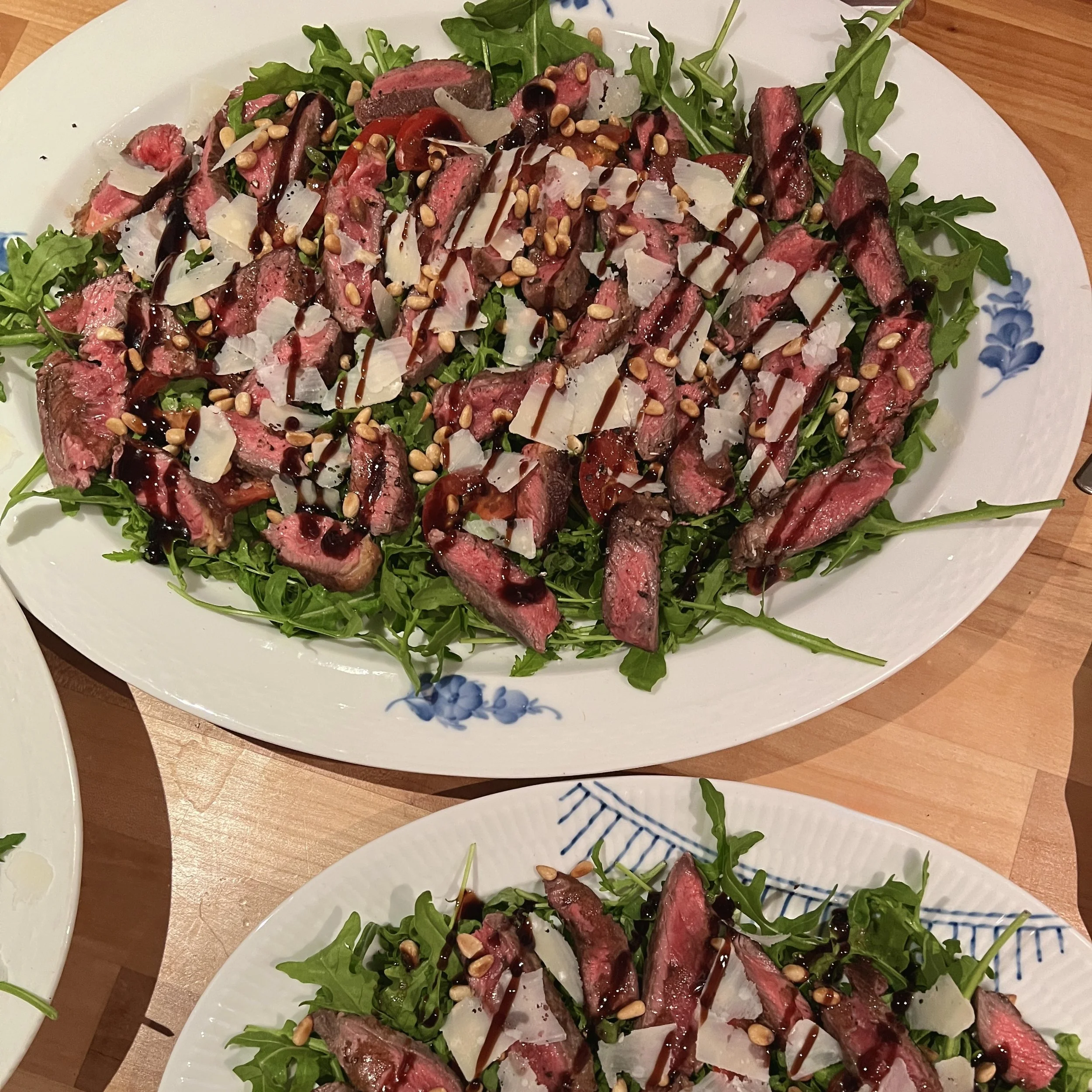 En tallerken med frisk grøn salat, skiver af rosa rødt kød, revet ost, pinjekerner og balsamico.