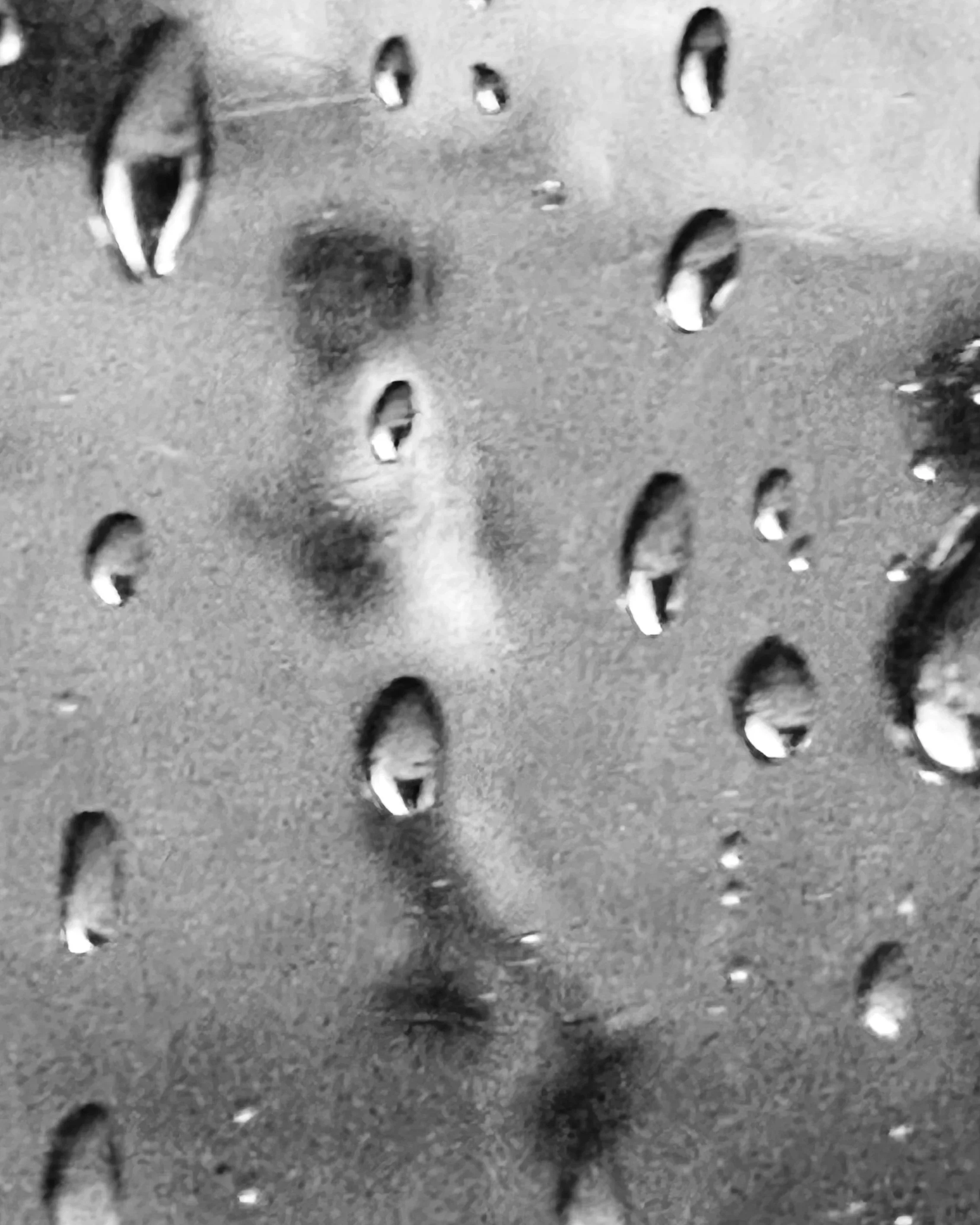Close-up of droplets of water on a textured surface, possibly glass or metal, with some droplets reflecting light.