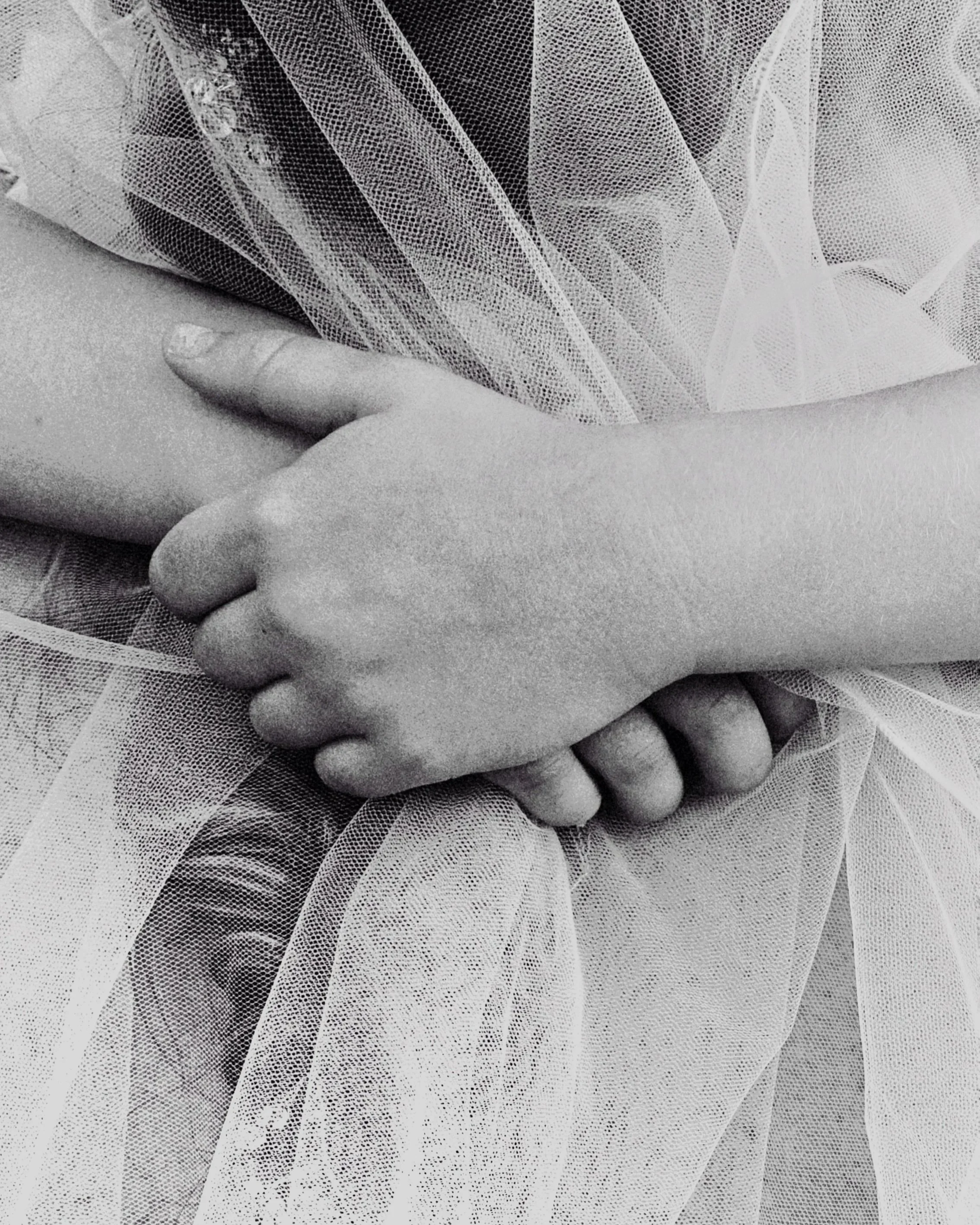 Close-up photo of two hands gently holding and touching a delicate, sheer fabric with intricate dot and line patterns.