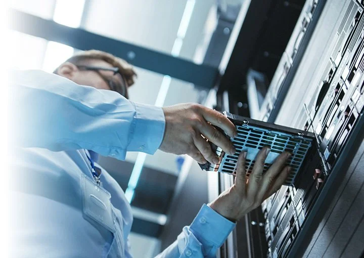 Person working inside a data center or server room, handling a server or hardware component.