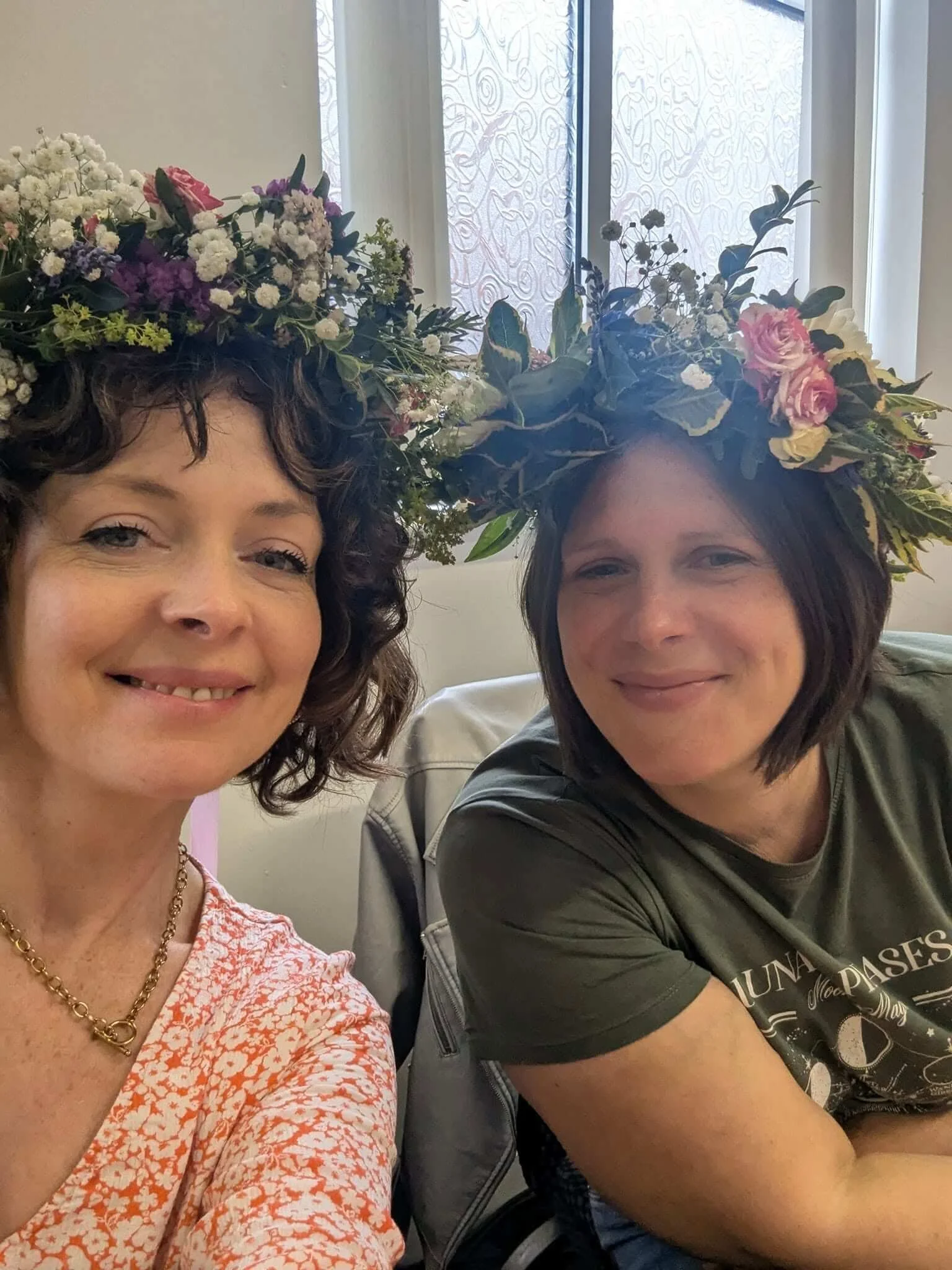 Two women wearing floral crowns, smiling at the camera