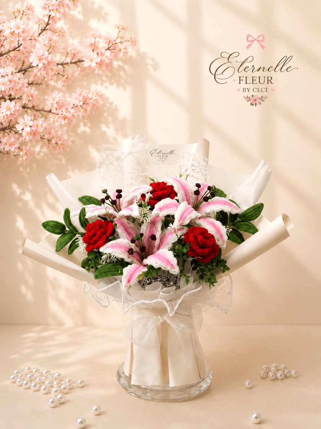 A floral arrangement featuring pink and white lilies, red carnations, and other greenery in gift wrapping, set on a beige surface with scattered pearls and a soft pink cherry blossom tree in the background. The branding 'Eternelle Fleur by Cece' appe