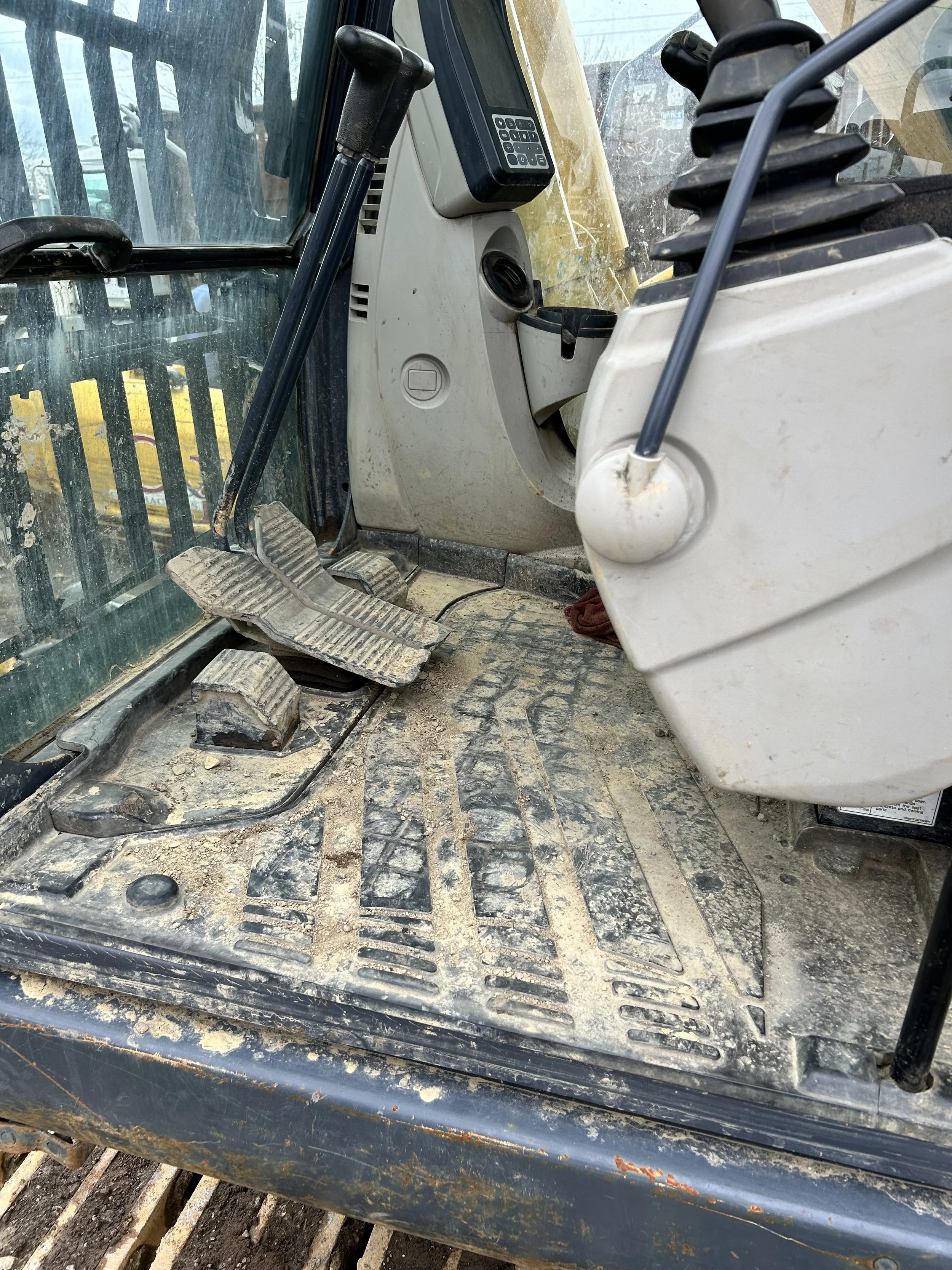 Close-up of a construction vehicle interior showing pedals, a control keypad, and part of the dashboard with dirty and worn surfaces.