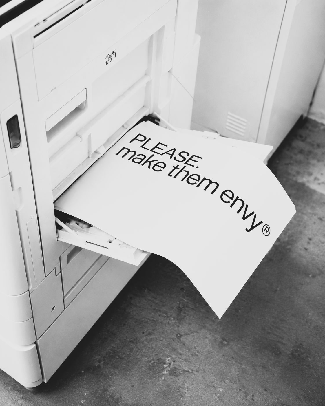 A large printer with paper displaying the text 'PLEASE. make them envy' being printed.