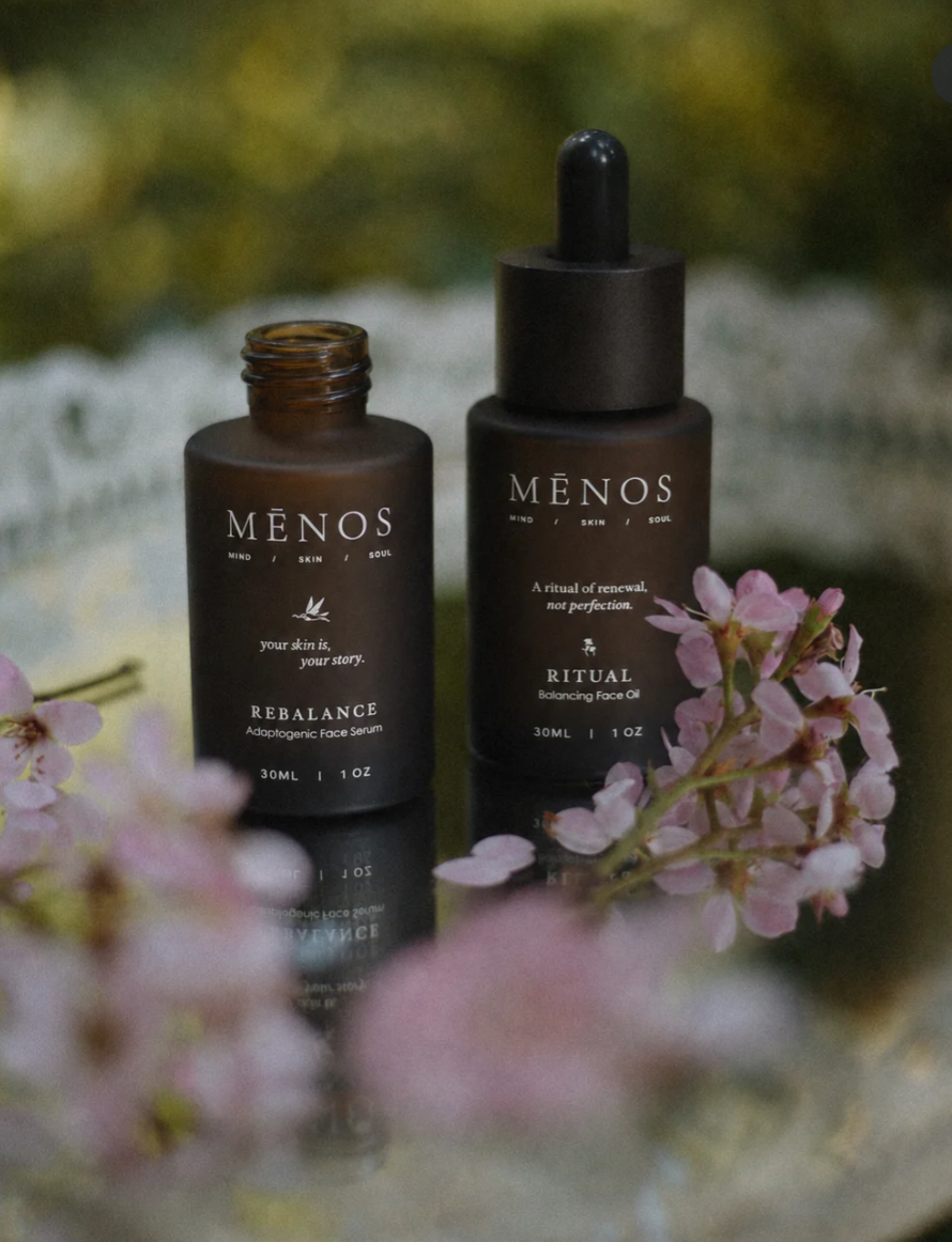 MĒNOS Rebalance face serum and Ritual face oil in amber glass bottles among pink blossoms