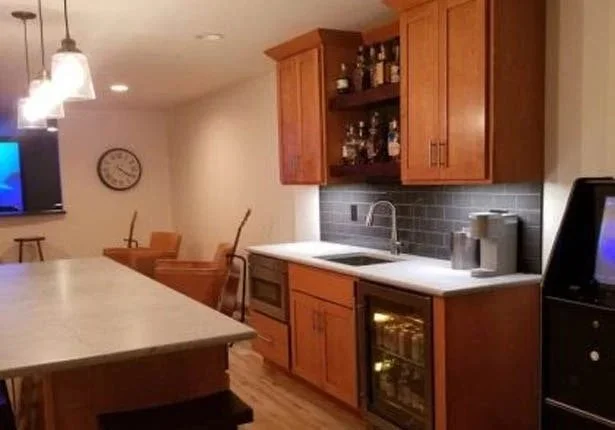 Kitchen with wooden cabinets, a white countertop, and a sink. Bar area with hanging lights and a television on the left. Four chairs are stacked on top of the counter.