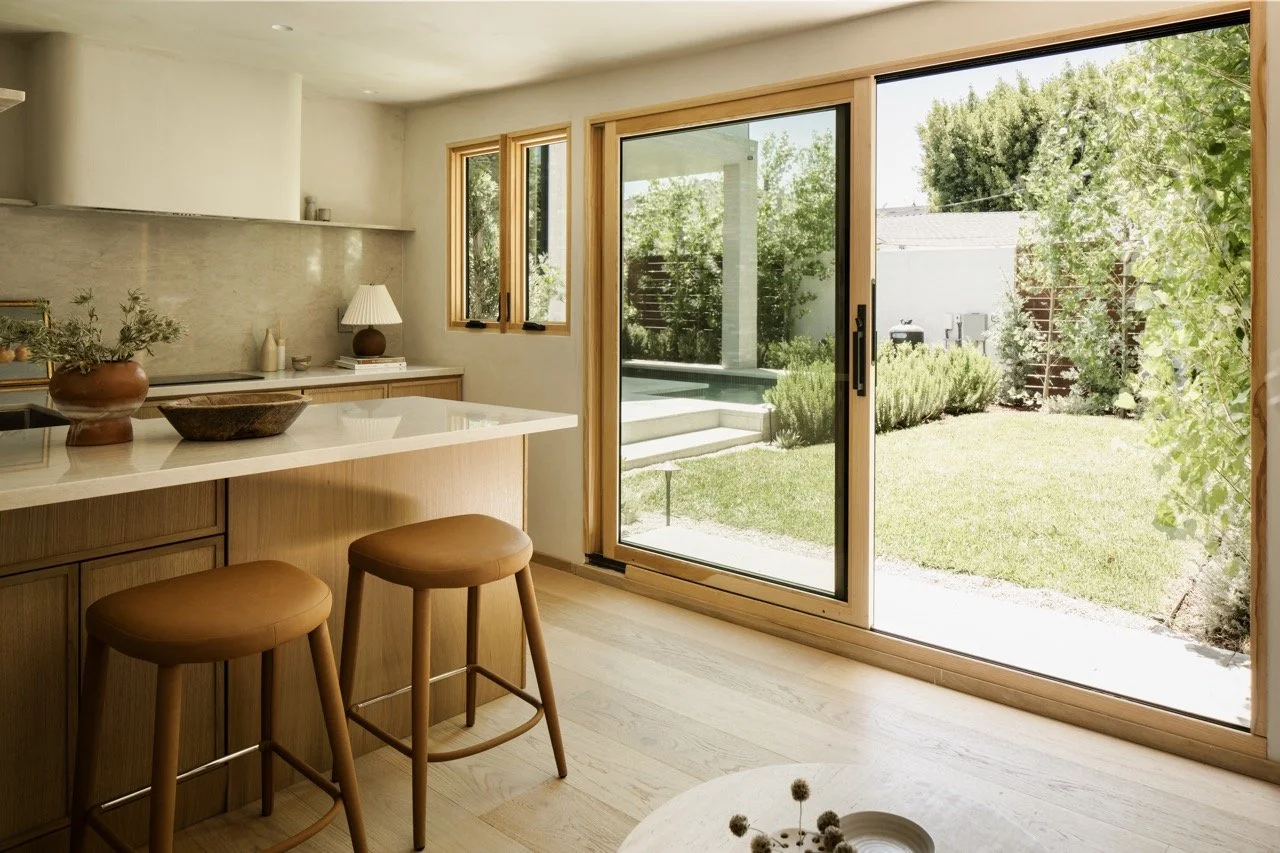 Bright kitchen with wooden cabinetry and a large glass sliding door leading to a green backyard with a lawn, shrubs, and trees.