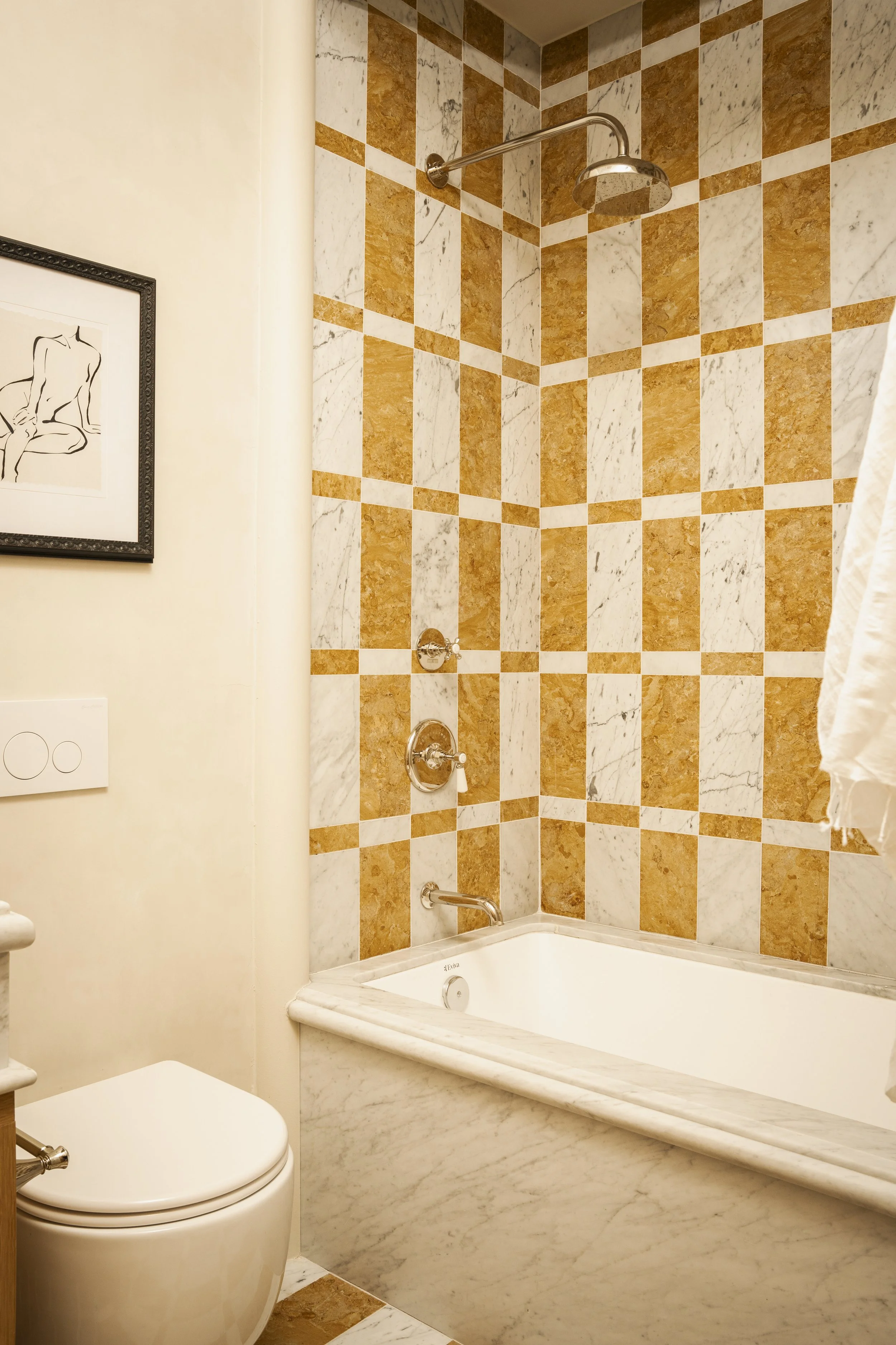 Bathroom with corner bathtub and marble surround, and a shower with brown and white checkered tiles. There is a framed artwork of a seated woman on the wall.