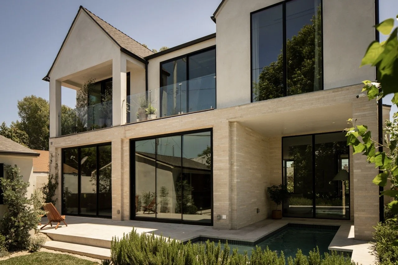Modern two-story house with large glass windows and sliding doors, outdoor patio, small pool, and landscaped garden.