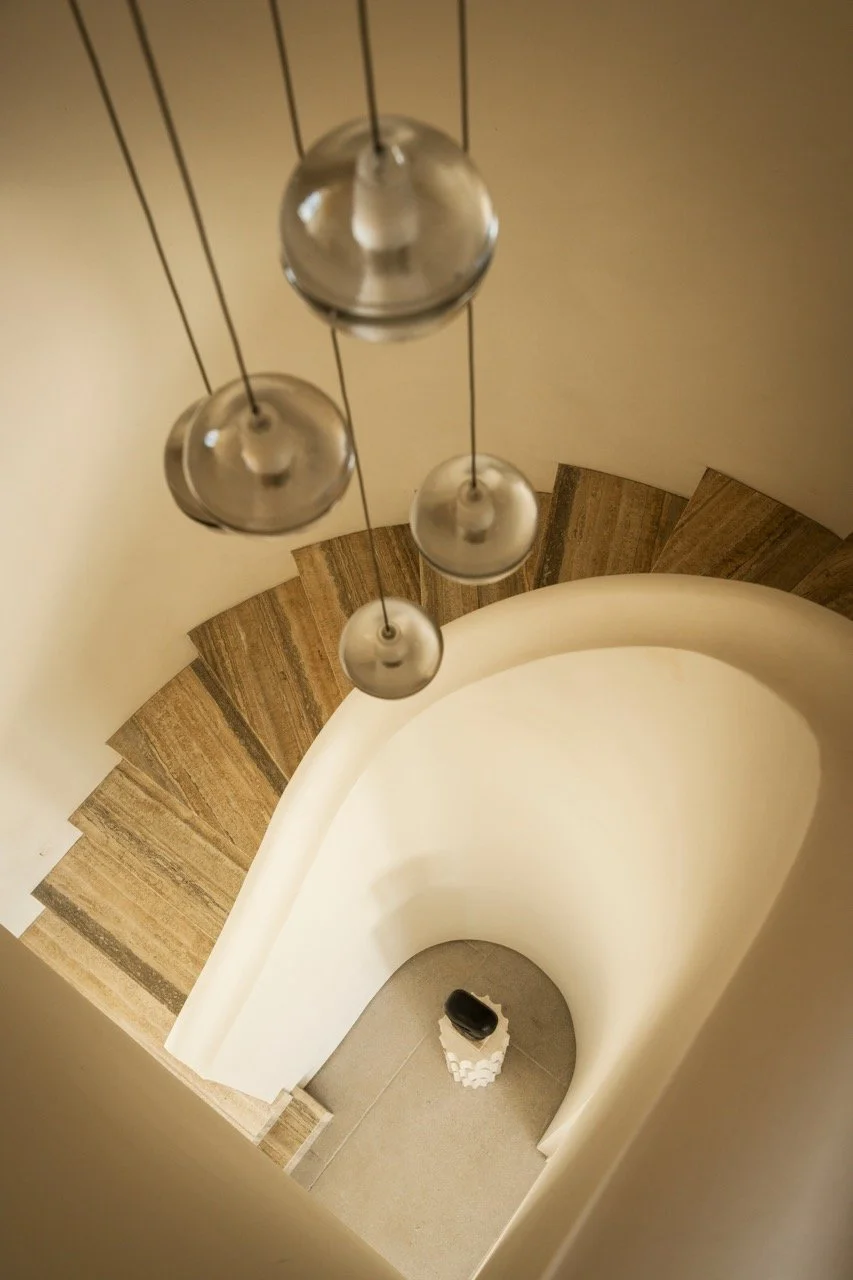 A spiral staircase viewed from above with a modern pendant light fixture hanging overhead and a toilet at the bottom.