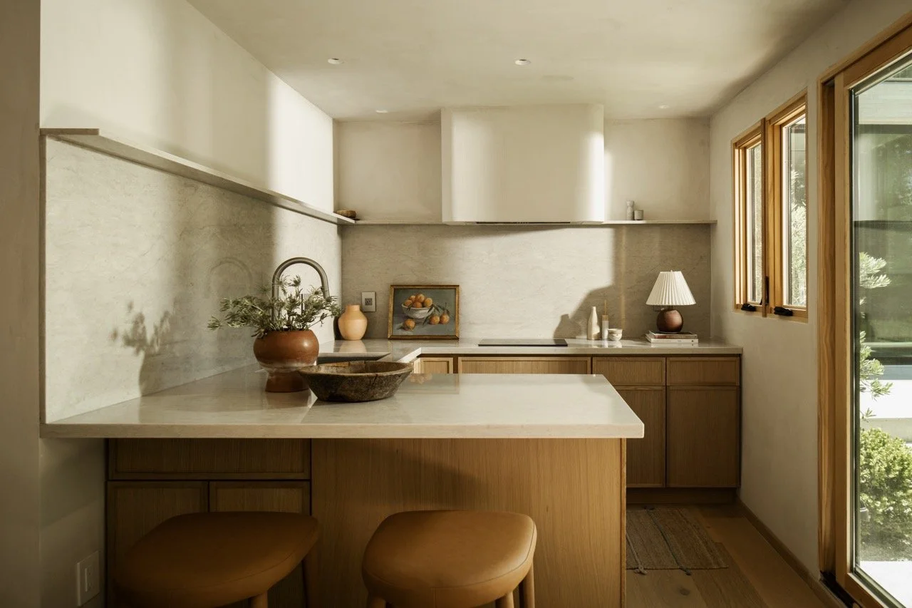 Minimalist kitchen with beige countertops, wooden cabinets, and large windows allowing natural light.