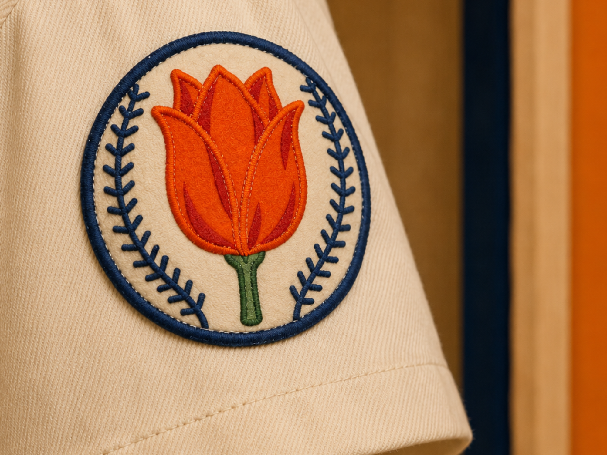 Close view of the Orange Wonders sleeve patch, with an orange-and-scarlet tulip inside a cream baseball edged and stitched in navy.
