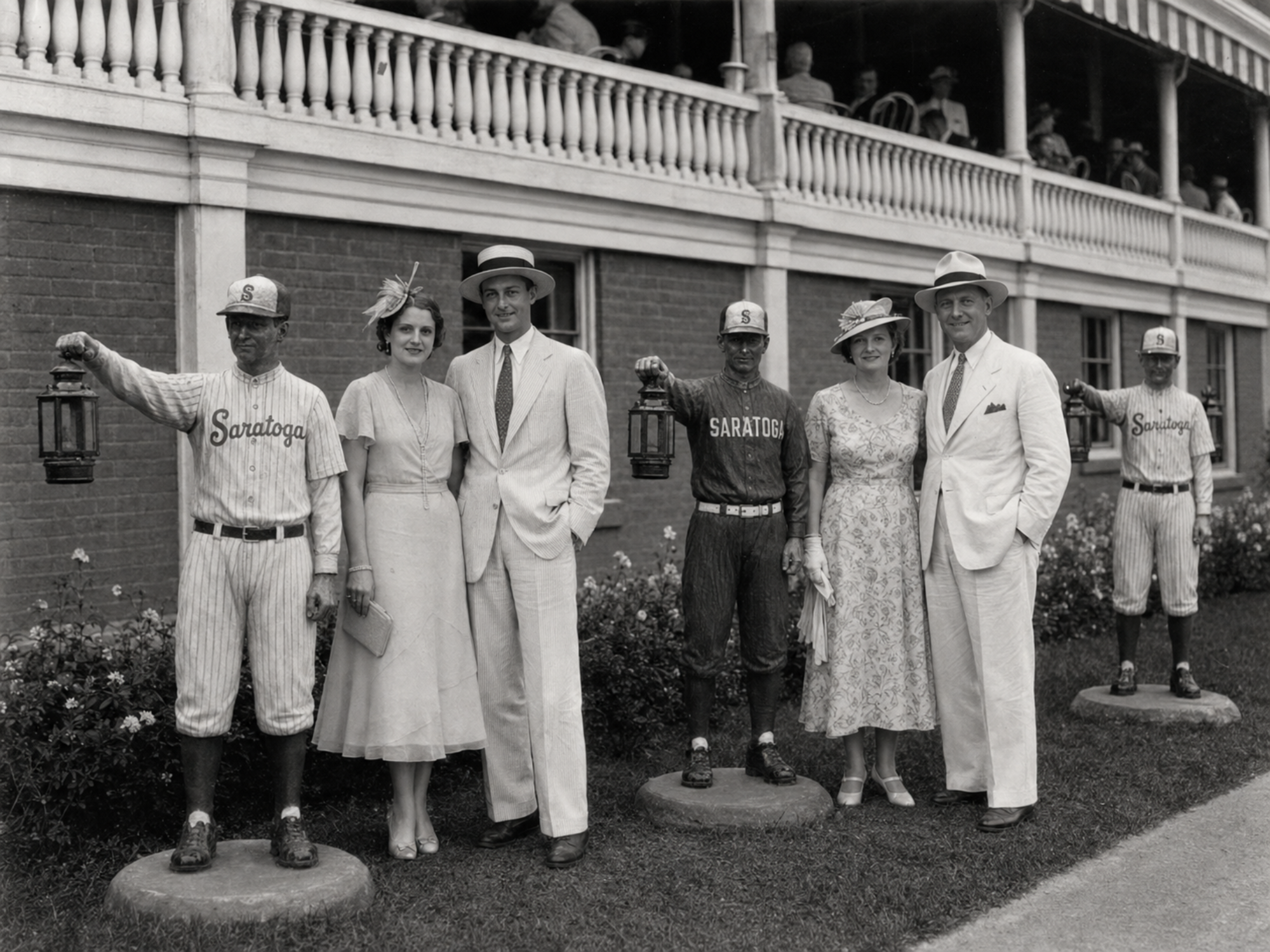 Two couples posing with three Fascinators lawn-jockey statues outside The Hatbox grandstand.