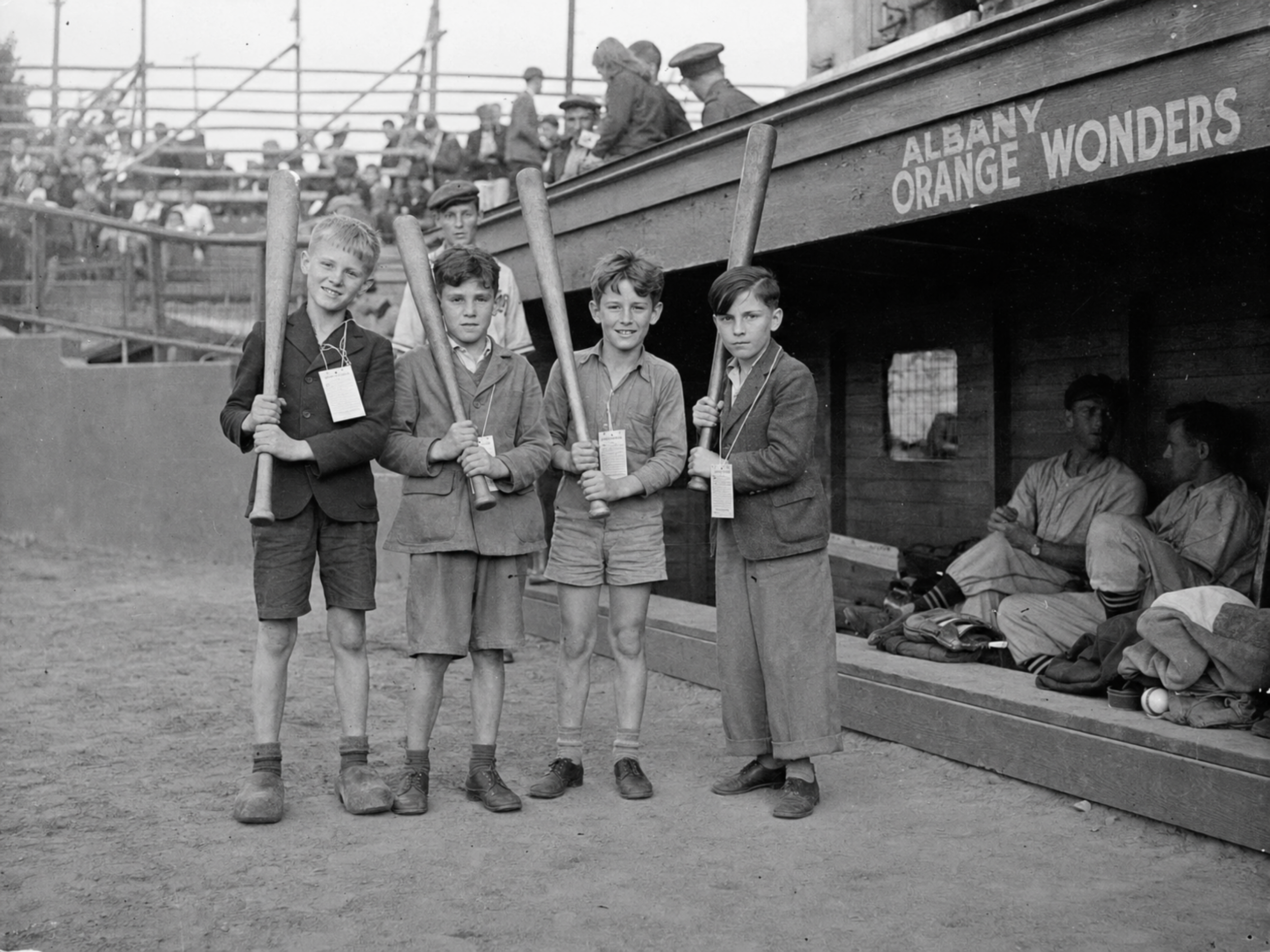 Black-and-white photograph of four Nijmegen boys holding baseball bats beside the Albany Orange Wonders dugout.