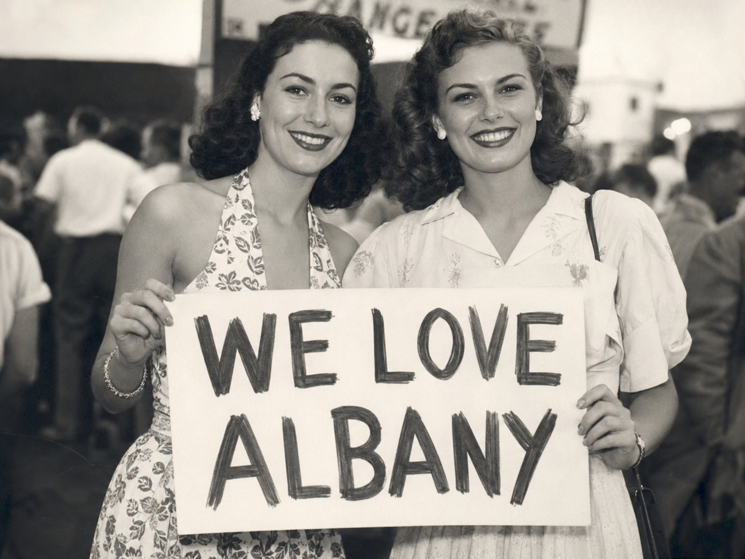 Black-and-white photograph of two women holding a “We Love Albany” sign at the Albany Orange Wonders sendoff.