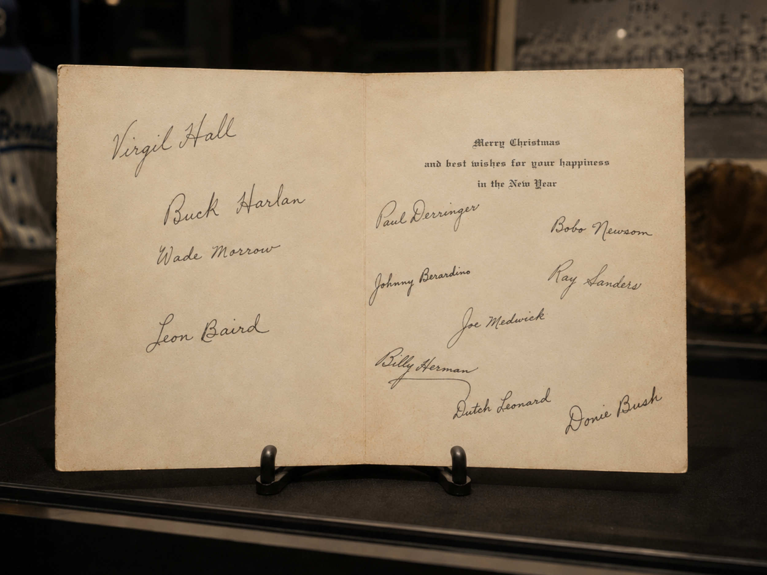 Museum display of an open 1936 Burnet Blue Bonnets holiday card with twelve team signatures.
