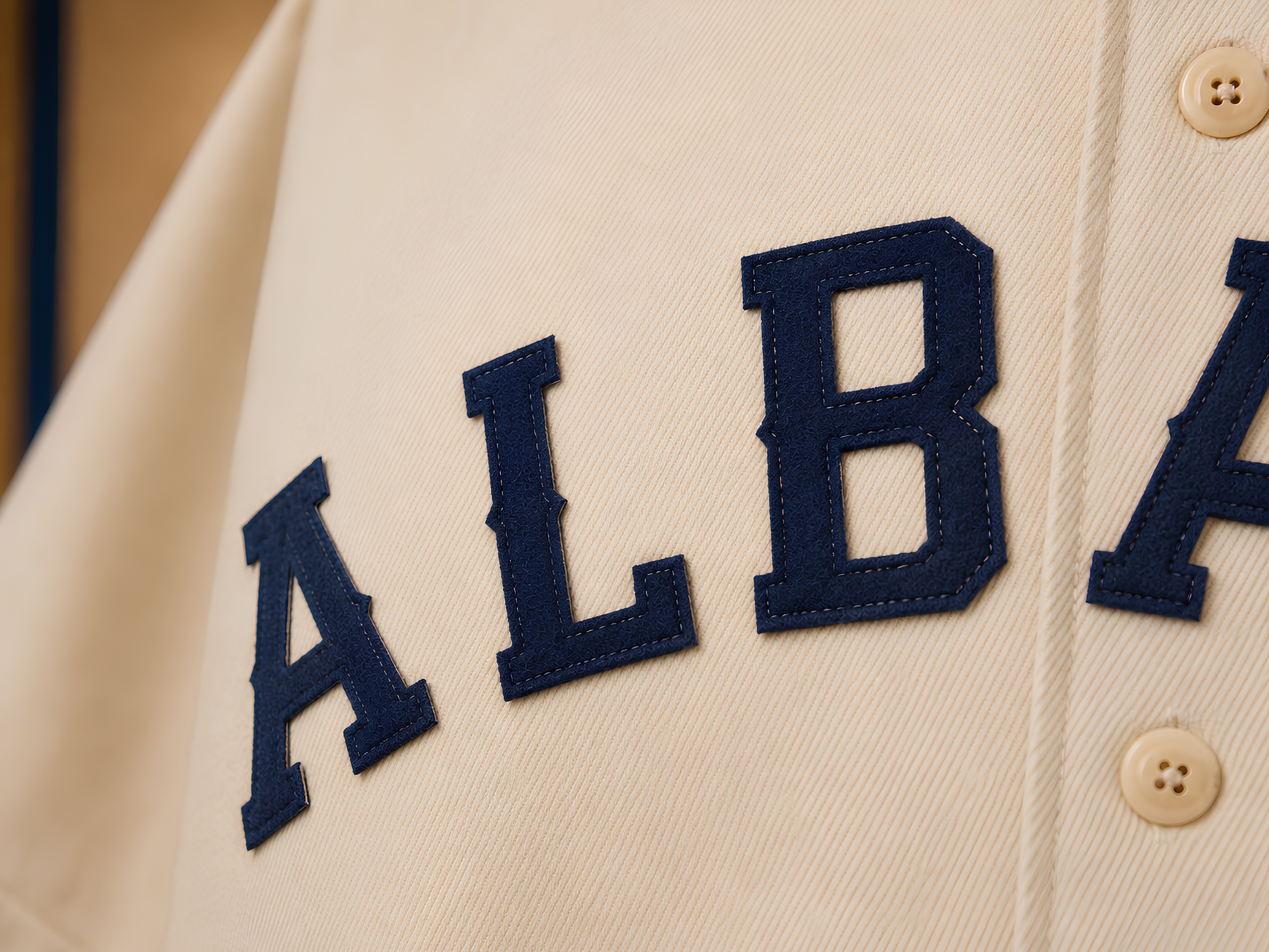 Close view of individually sewn, notched Dutch navy ALBANY felt letters on the cream Orange Wonders jersey.