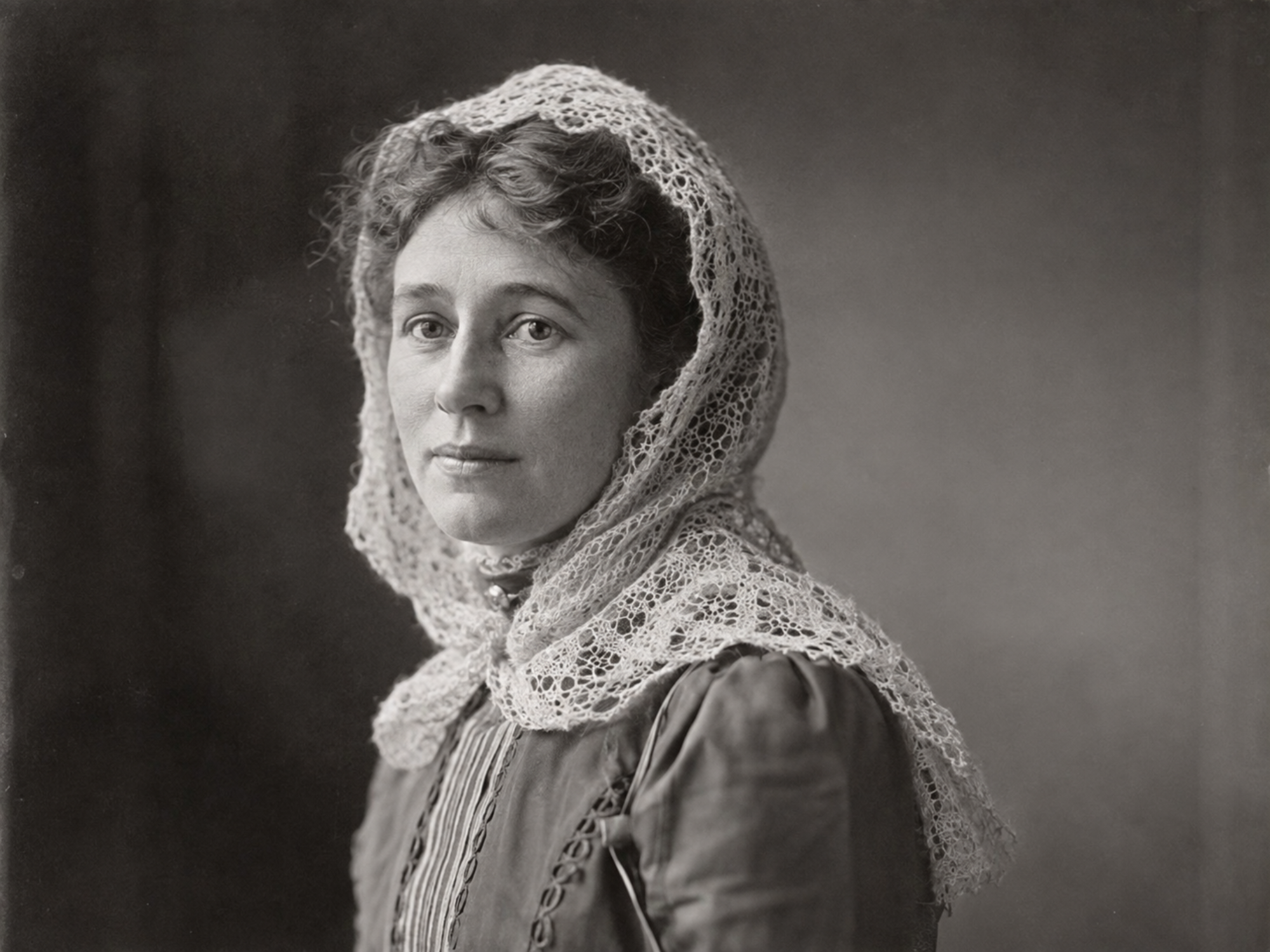 Woman wearing a lace hood-style fascinator around her head and shoulders in 1890.
