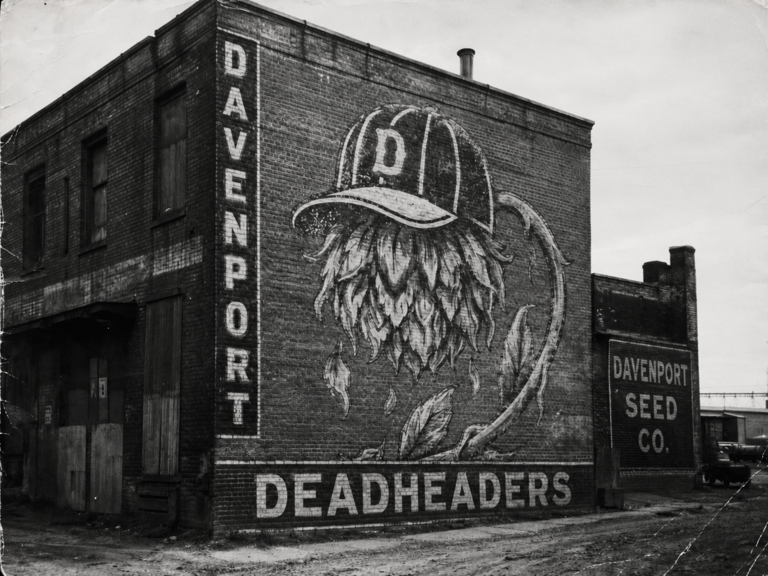 Black-and-white 1940s photograph of a brick Davenport warehouse with a large faded Davenport Deadheaders mural painted on the wall.