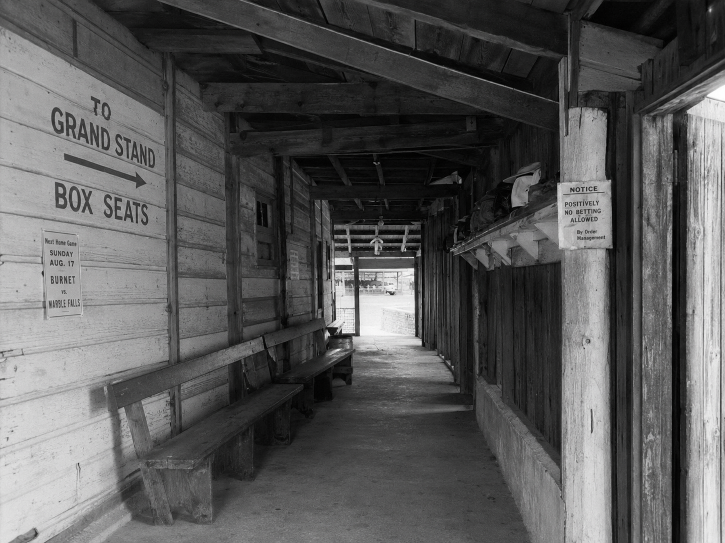 Black-and-white 1940s photograph of a wooden passageway beneath the Fair Grounds Park grandstand, with signs pointing toward box seats and the grandstand.