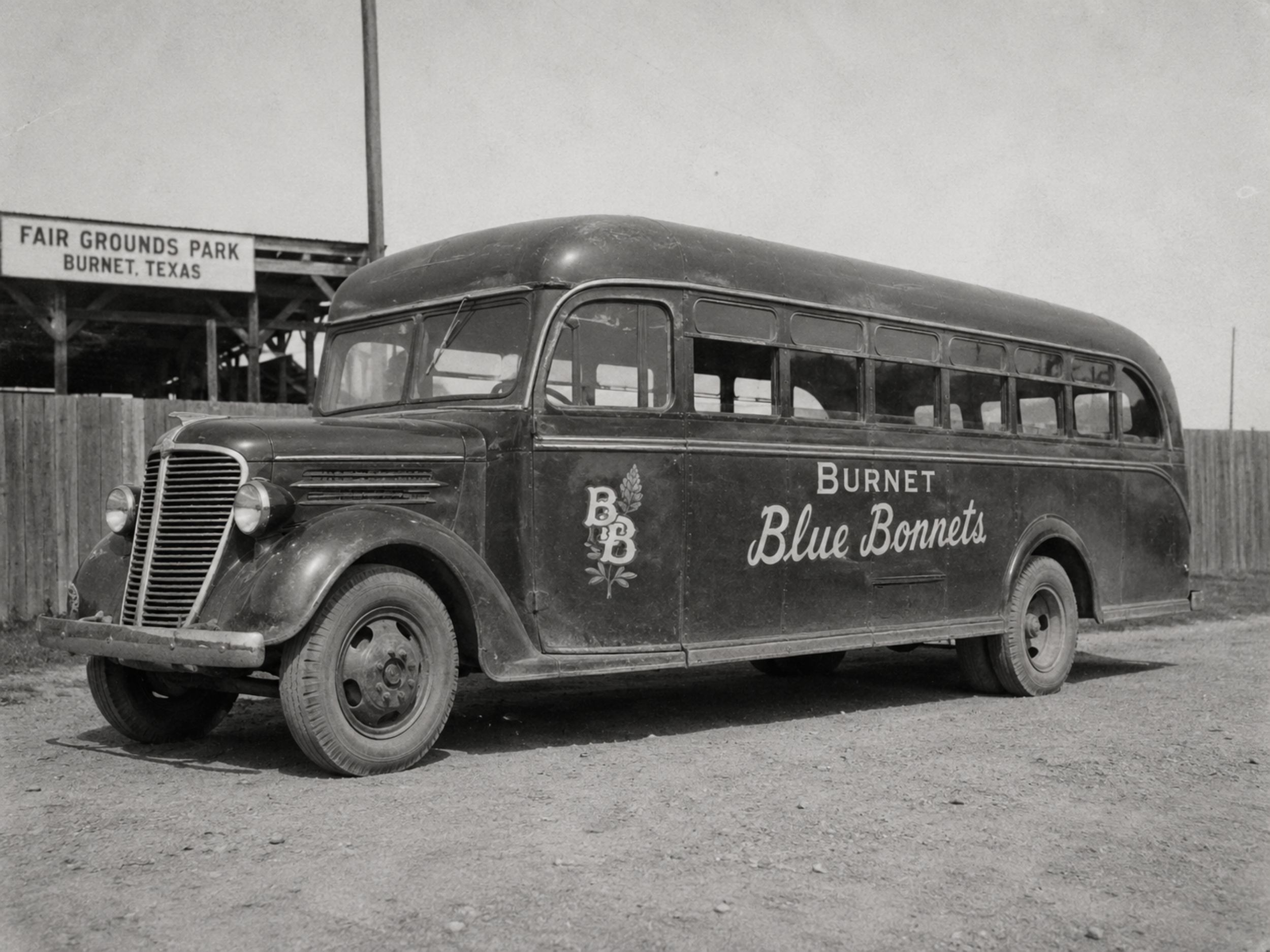 Black-and-white 1940s photograph of the Burnet Blue Bonnets team bus parked outside the Fair Grounds Park fence with club lettering painted on the side.