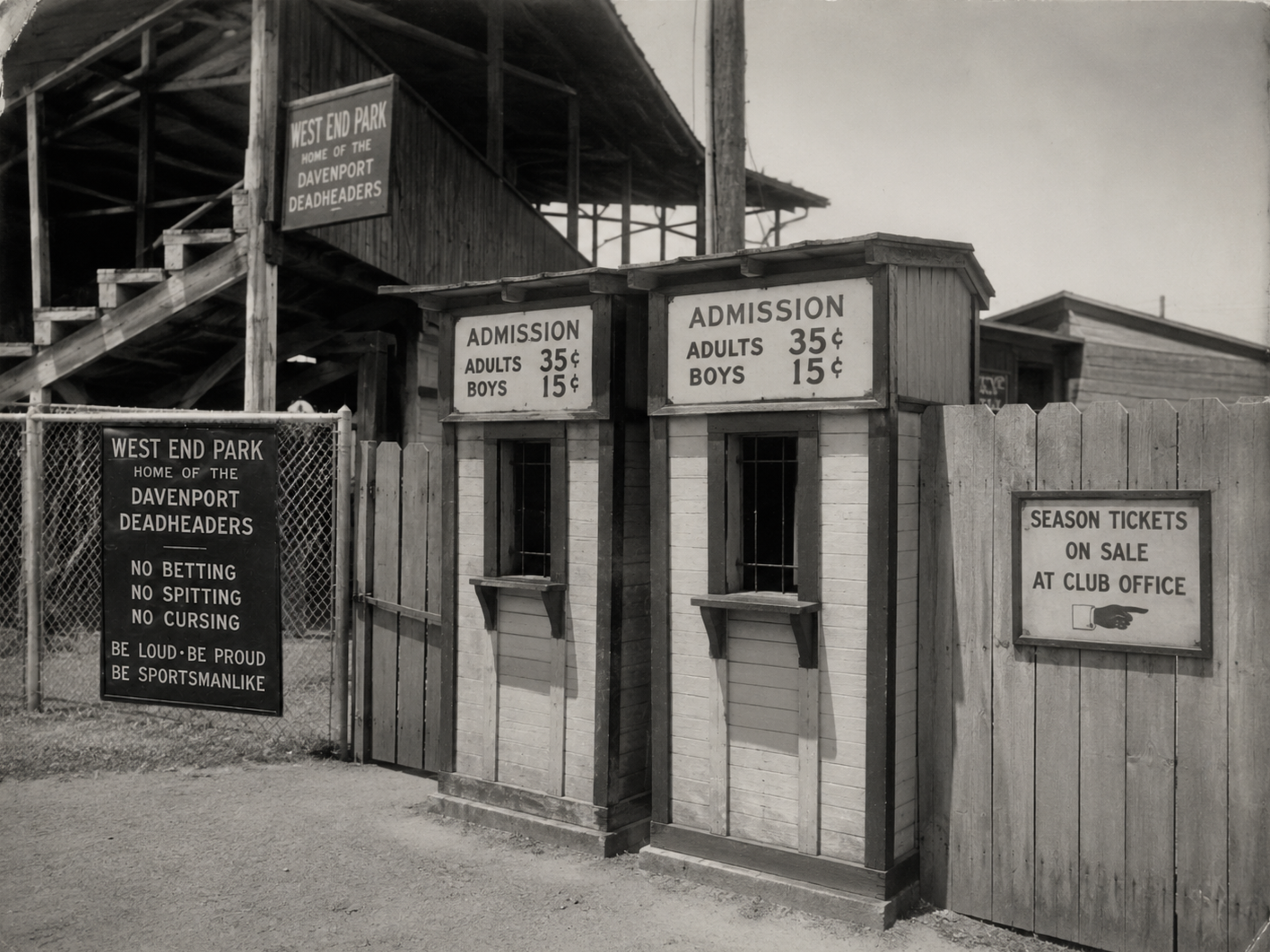 Two West End Park ticket booths with barred admission windows, posted price boards, and wooden fencing near the ballpark entrance.