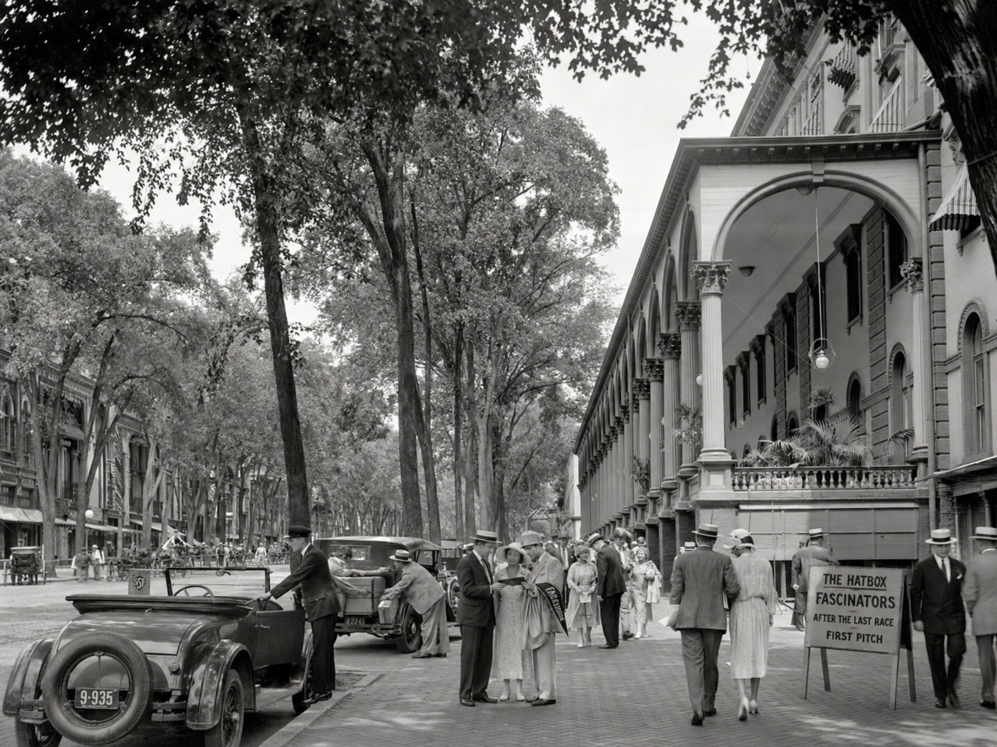Pedestrians outside the Grand Union Hotel pass a sidewalk placard advertising a Fascinators game after the final race.