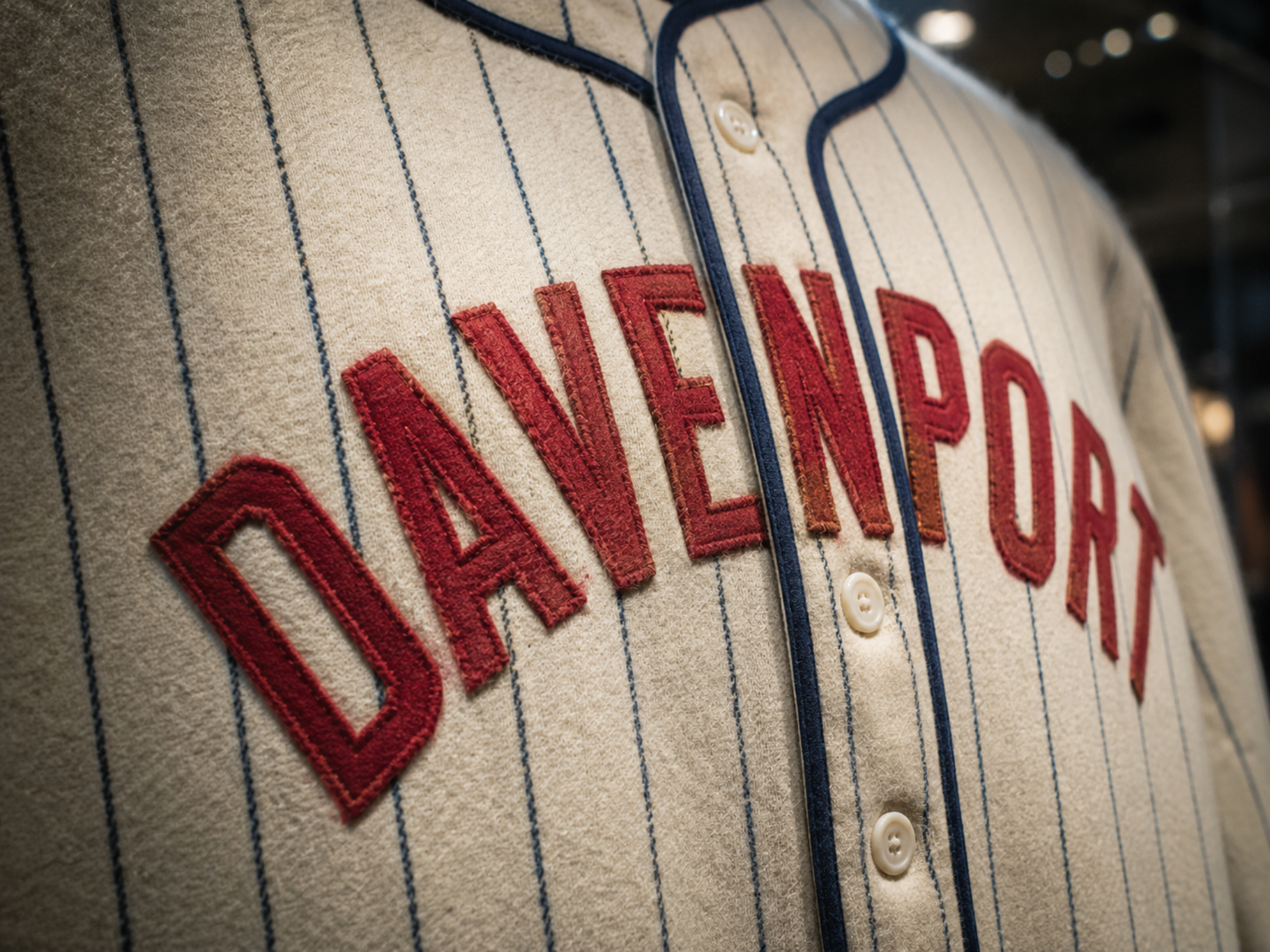 Close-up museum photograph of the Davenport Deadheaders’ primary uniform, showing red stitched DAVENPORT lettering across a cream flannel jersey with navy pinstripes, navy trim, and a button front.