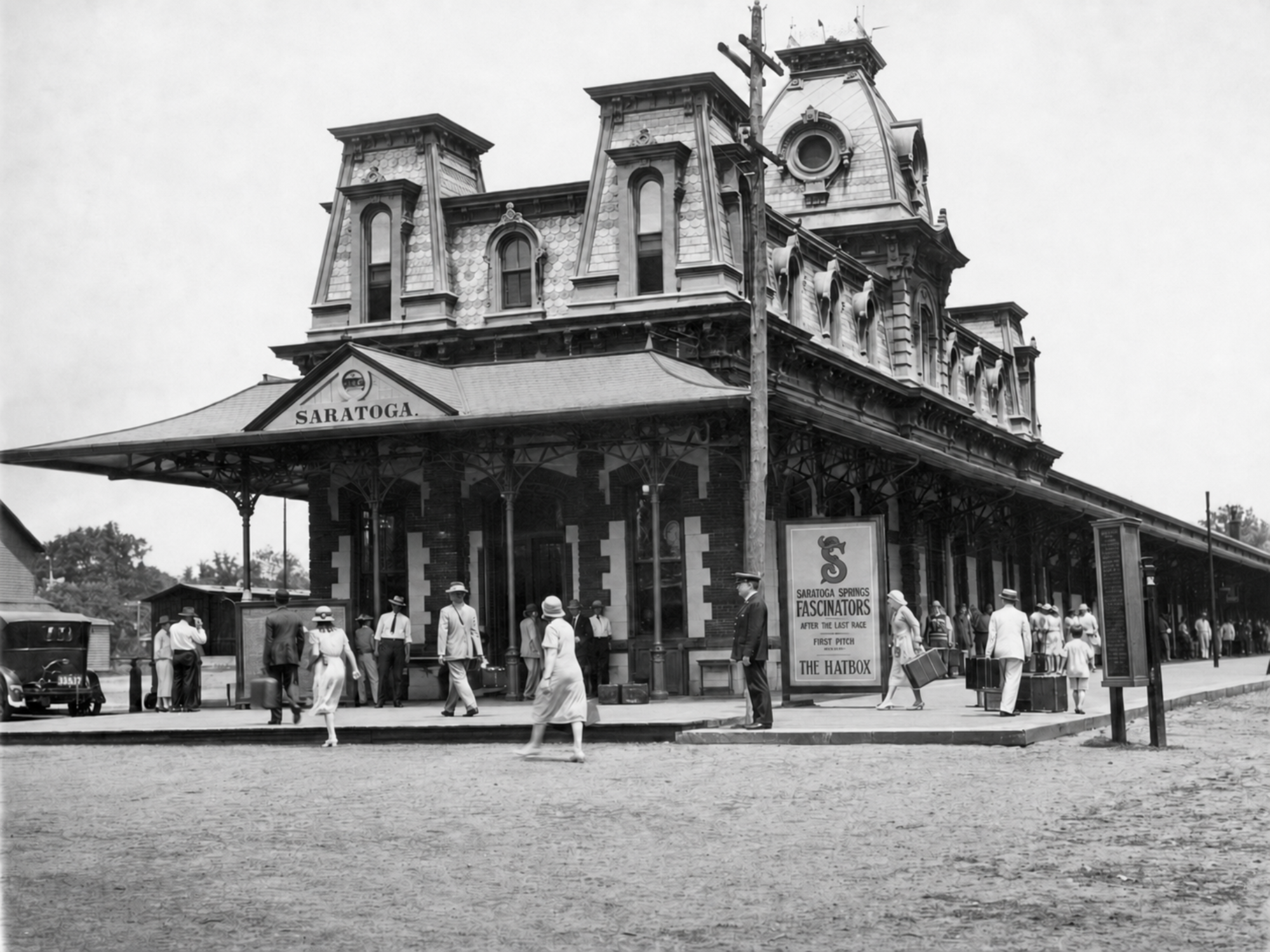 Travelers outside the Saratoga Springs train station pass a painted notice promoting the Fascinators and The Hatbox.
