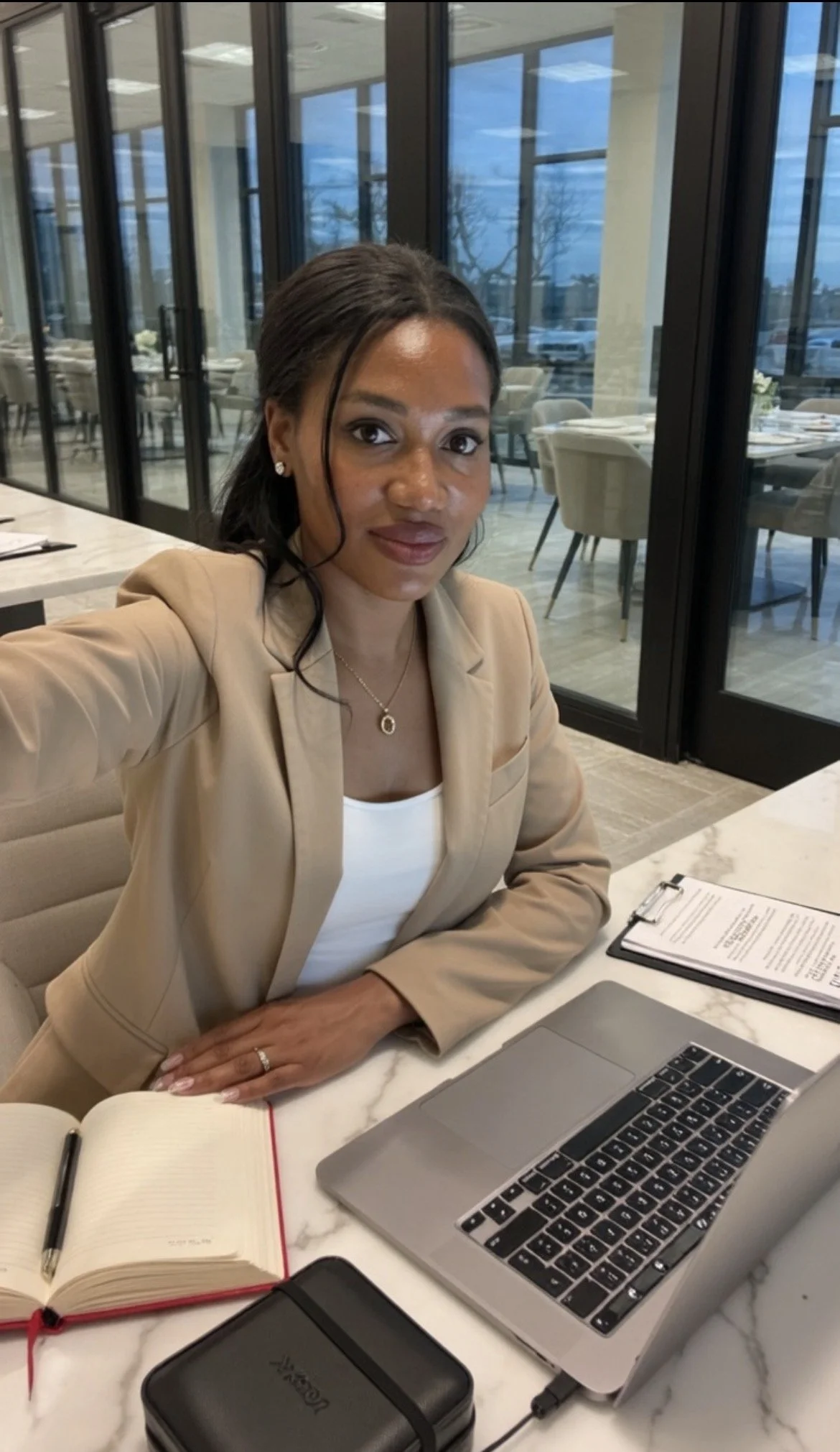 Sanjanetta Barnes working at a desk, wearing a tan blazer and white top,