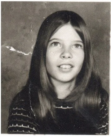Black and white photo of a young girl with long straight hair, wearing a dark sweater with horizontal stripes.