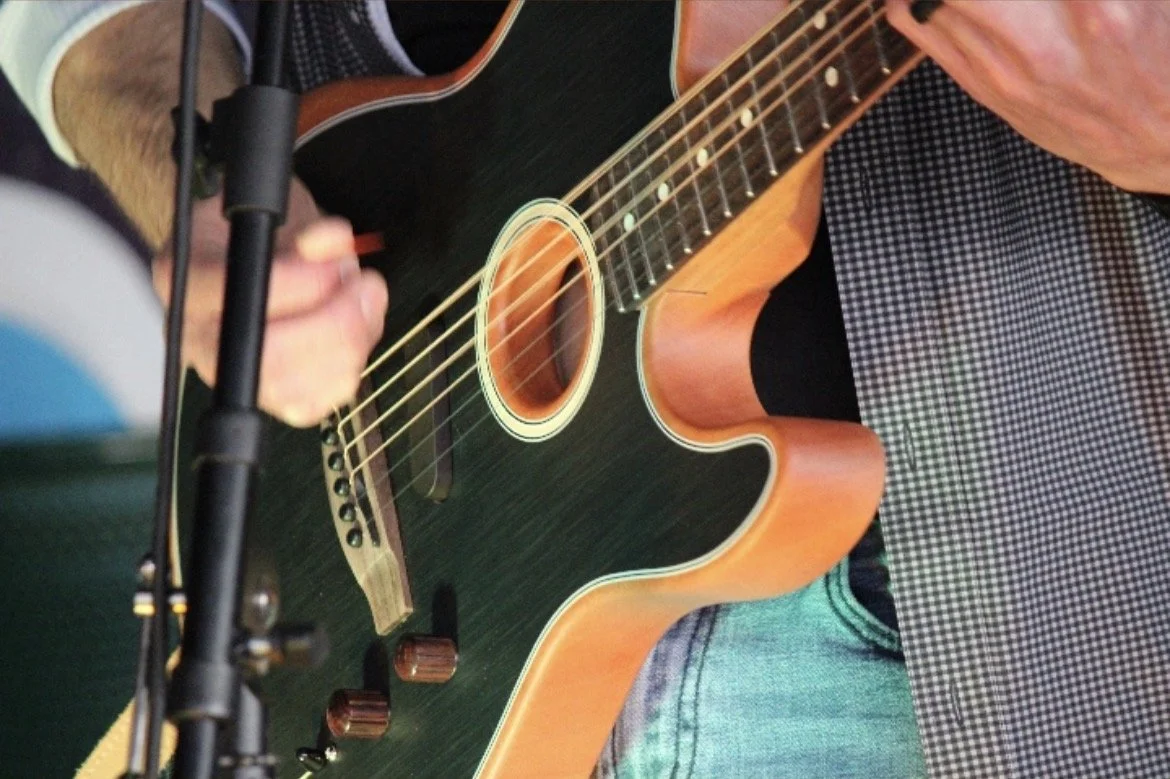 Person playing an acoustic guitar with a microphone nearby.