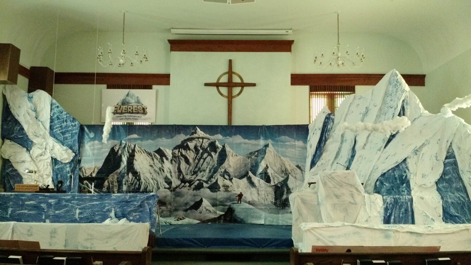 Indoor scene depicting a mountain-themed decoration with painted backdrop of snow-capped peaks and artificial ice formations in the foreground.