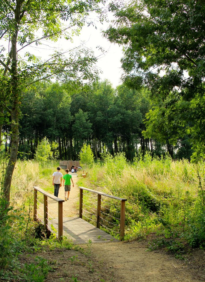 Deux enfants marchent sur un petit pont en bois dans une forêt verdoyante.