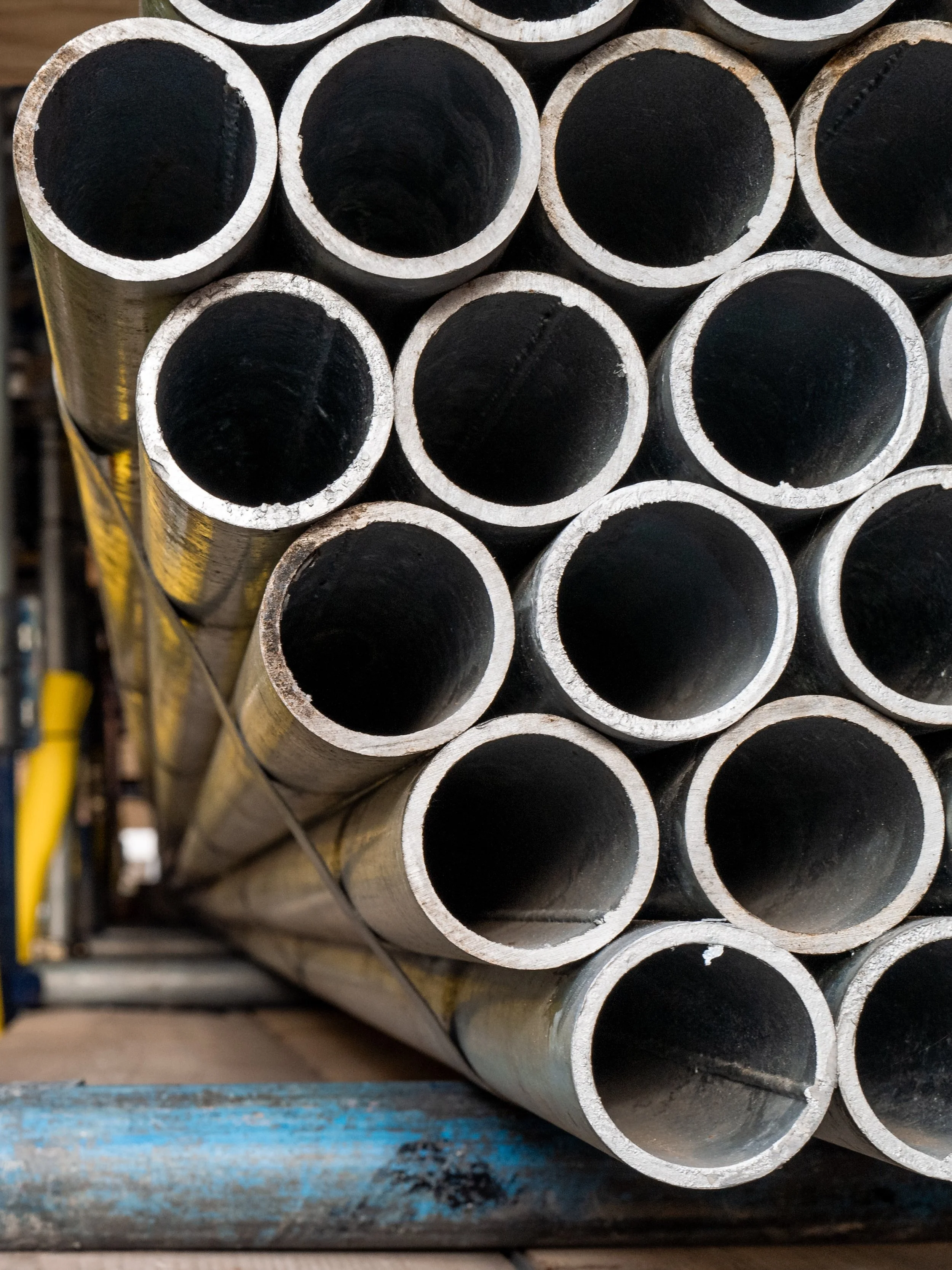 A stack of metal pipes arranged in a rectangular pattern on a blue wooden surface in an industrial setting.