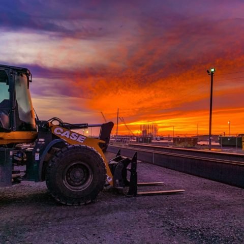 A CASE front loader parked on a construction site during a vibrant sunset with orange and purple sky.