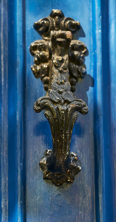 Close-up of an ornate black metal door knocker on a blue door