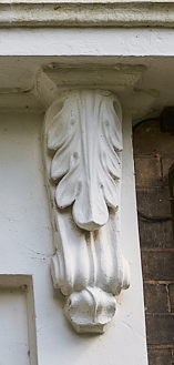 Close-up of an ornate white architectural corbel with leaf and scroll motifs supporting a building's overhang.