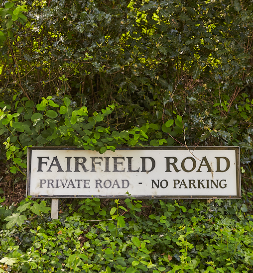 Sign for Fairfield Road, a private road with no parking, surrounded by greenery and bushes.