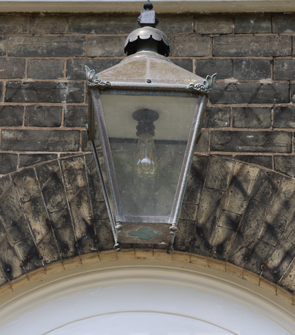Outdoor lantern attached to a brick wall above an arched doorway.