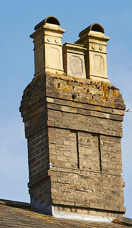 Close-up of a brick chimney with two white decorative chimney pots on top, set against a blue sky.