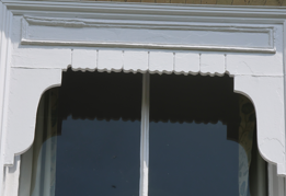 Close-up of a window with decorative white trim against a white wall