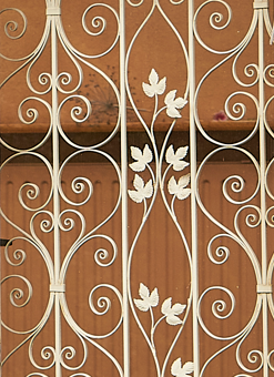Decorative white wrought iron gate with intricate scrollwork and leaf patterns, set against a wooden background.