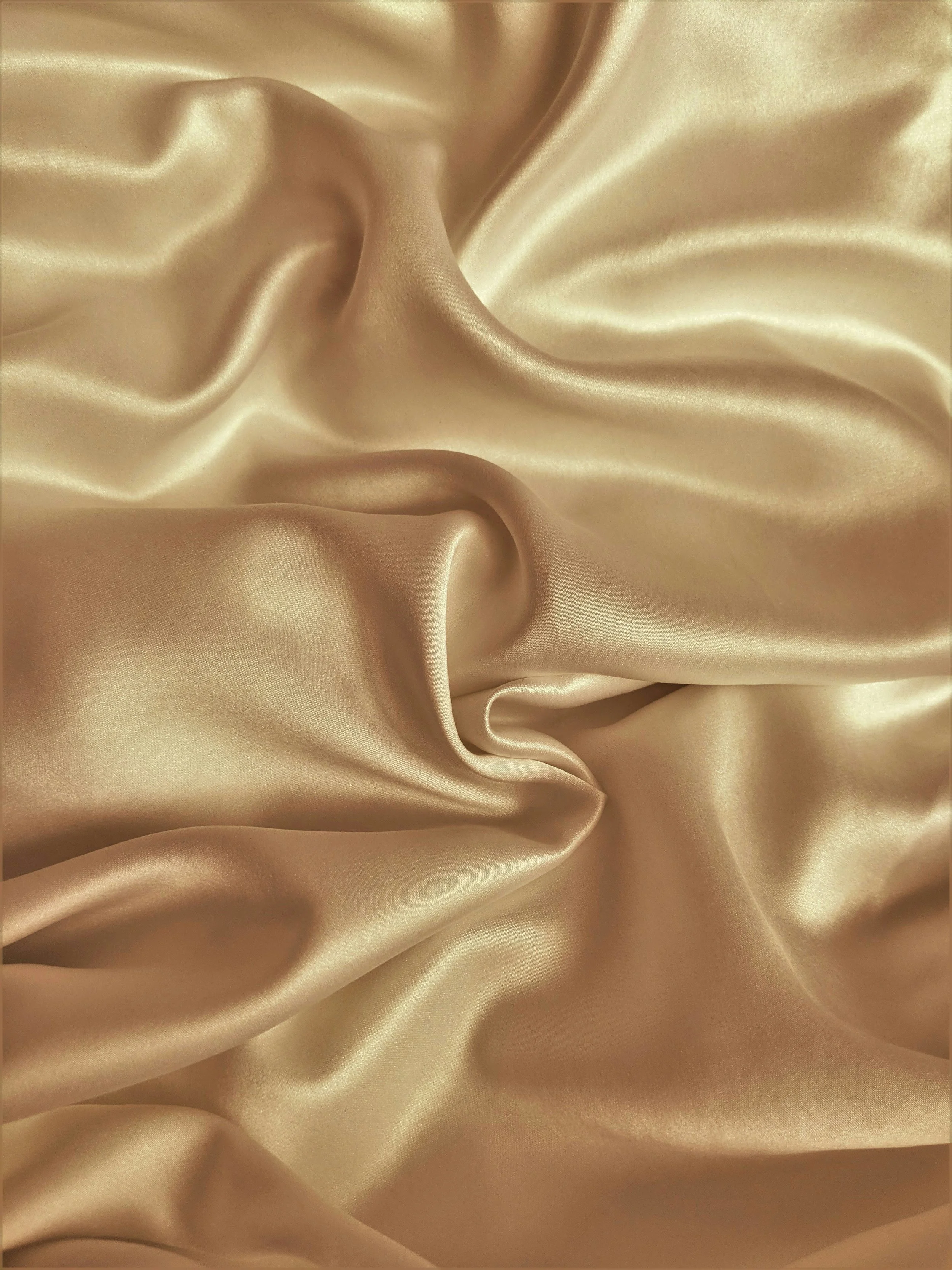 Close-up of beige shiny satin fabric with folds and smooth texture.
