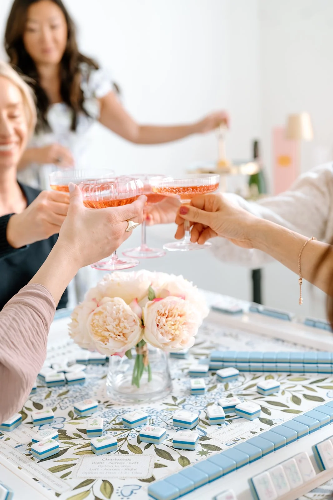 Group of women toasting with pink cocktails at a table with a floral centerpiece and a game of Mahjong.