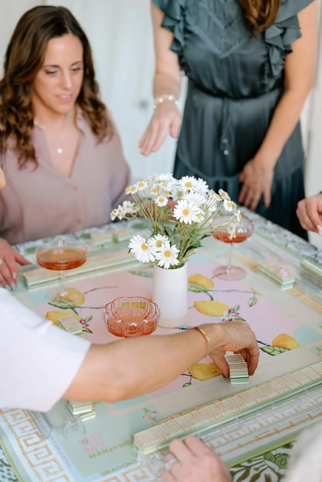 People playing a board game at a table decorated with a vase of daisies and pink drinks.