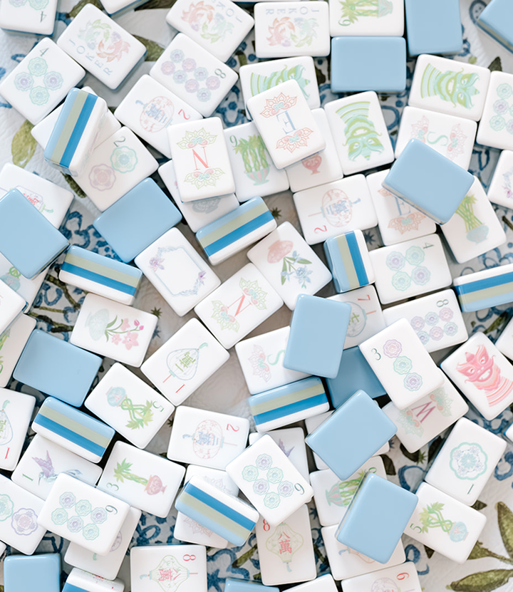 A close-up of a pile of Mahjong tiles, featuring various symbols, characters, and designs in white, blue, and pastel colors.