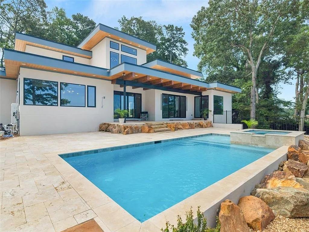 Modern house with large windows, a swimming pool, and a hot tub in the backyard, surrounded by trees.
